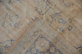 Distressed Oushak rug corner: worn cream pile, pale blue patterns, and tan foundation.
