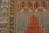 Distressed Anatolian rug close-up: red prayer arch, denim blue field, and pale floral panels.