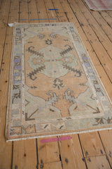 Distressed Oushak rug corner, featuring worn pile, dusty gold field, and geometric pale blue spandrel.