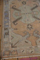 Distressed Oushak runner's worn pile texture, serrated motifs, and border in faded gold, pale blue.