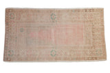 Vintage distressed Oushak prayer rug with a soft pink field and sand geometric border.