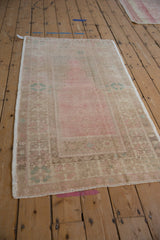 Angled view of a distressed Oushak prayer rug with a low pile and soft pink and sand tones.