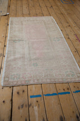 Angled view of a vintage Oushak prayer rug with a faded pink field and geometric border.