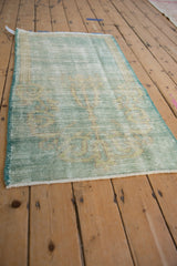 Distressed mint green Oushak rug corner shows worn pile, faded prayer design, and intact side selvage.