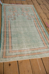 Angled view of a distressed Oushak rug with a striped gold border and mint green field.