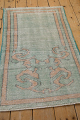 Angled perspective on a distressed vintage Oushak rug highlighting its scrolling vine motif and texture.
