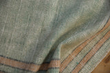 The worn, hand-knotted texture of a pale mint green Oushak rug with dusty gold stripes.