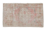 A distressed vintage Oushak rug with a faded pink medallion on a sandy beige field with worn texture.