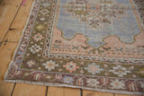 Angled view of a vintage Oushak corner showing the worn texture and stylized checkered border.