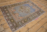 Vintage distressed Oushak rug from an angle, showing time-softened blue, sandalwood, and olive tones.