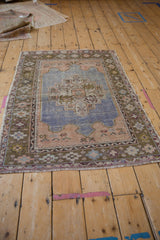Vintage distressed Oushak rug with a faded blue medallion, seen from an angled perspective.