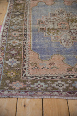 Worn hand-knotted texture on the checkered and meandering vine borders of a vintage Oushak rug.
