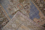 Flipped corner of a distressed Oushak rug showing its hand-knotted foundation and low pile.