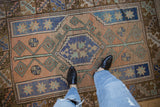 Distressed Melas rug showing faded terracotta field, blue pinwheel starbursts, and geometric patterns.