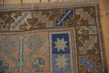 Distressed Melas rug corner with fringe, featuring blue pinwheel starburst and banded vinery.