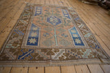 Distressed Melas rug close-up: worn texture, faded terracotta, stylized ram's horn tendrils in border.