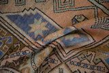 Distressed Melas rug close-up showing blue pinwheel starbursts, terracotta, and mint green geometry.