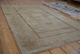 Faded beige and sand distressed texture on a vintage Oushak rug with dark geometric border.