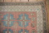 Distressed Oushak rug corner showcasing pale ruby, denim blue guls and ivory geometric border.