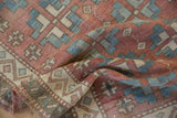 Distressed Oushak rug corner showing zig zag vine and seed border motif in blush, ivory, blue.