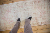Distressed Oushak runner with worn pile, displaying faded ivory, pink, and beige patterns.