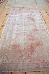 Angled view of a vintage Oushak runner showing decorative wear over a raspberry red and ivory pattern.