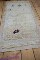 Distressed vintage Tulu runner featuring shaggy cream pile with primitive animal and plant motifs.