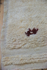 Shaggy cream Tulu rug pile with dark primitive relief design and flatwoven edge.
