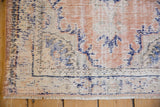 Corner of a distressed Oushak rug showing worn-down pile in dusty apricot and cobalt blue.
