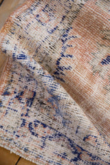 The worn, hand-knotted pile of a distressed Oushak rug in dusty apricot and cobalt blue.
