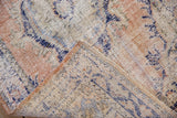 Folded corner of a distressed Oushak rug revealing its hand-knotted pile and foundation.