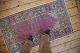 Distressed Oushak rug runner with a purple prayer design, shown for scale on a wooden floor.