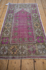 Full angled view of a distressed Oushak prayer rug with a purple field and decorative floral border.