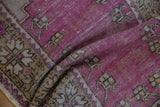Detail of a vintage Oushak rug's serrated palmette border and distressed purple wool pile.
