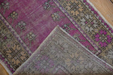 A folded corner reveals the hand-knotted weave on the back of this vintage purple Oushak rug.