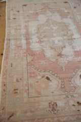 Side view showing the distressed, low-pile texture and dusty rose border of the vintage Oushak rug.