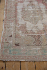 Angled corner view of a distressed Oushak rug showing exposed foundation and faded dusty rose pile.