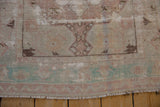 End of a distressed Oushak rug with worn pile, ivory fringe, and pale blue-green border.