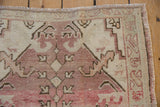 Distressed vintage Oushak rug corner with faded rose patterns, worn pile, and selvage.