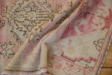 Abrashed texture of the distressed Oushak rug, with faded rose, beige, and intact fringe.