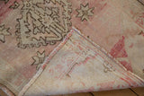 Distressed Oushak rug with faded rose and beige pile, showing woven foundation.