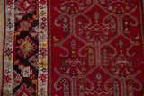 Close-up of the geometric charcoal border and samovar panels on a red field.