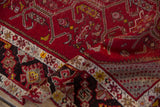 Intricate scrolled vine and samovar details on the cherry red pile of a folded vintage Turkish runner.