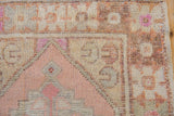 Vintage Oushak rug border with distressed pink, cream, and orange geometric pattern.