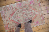 Distressed Oushak rug corner showing low pile, seed trellis spandrel, and faded pink-rust hues.