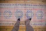 Vintage distressed Oushak runner, dusty pink field with cobalt blue starburst medallions and visible wear.