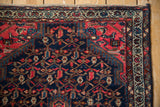 Tajabad rug corner with cherry red field, navy scrolling vinery, botehs, and an ivory border.
