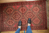 Feet on vintage Belouch rug, highlighting raspberry red and dusty aubergine geometric guls.