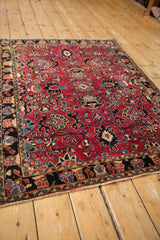Vintage Sarouk rug's cherry red field, navy border with floral motifs, and tattered edge.