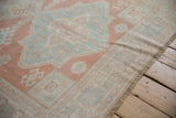 Distressed Oushak rug texture highlighting cantaloup, ivory, and pale mint floral motifs.